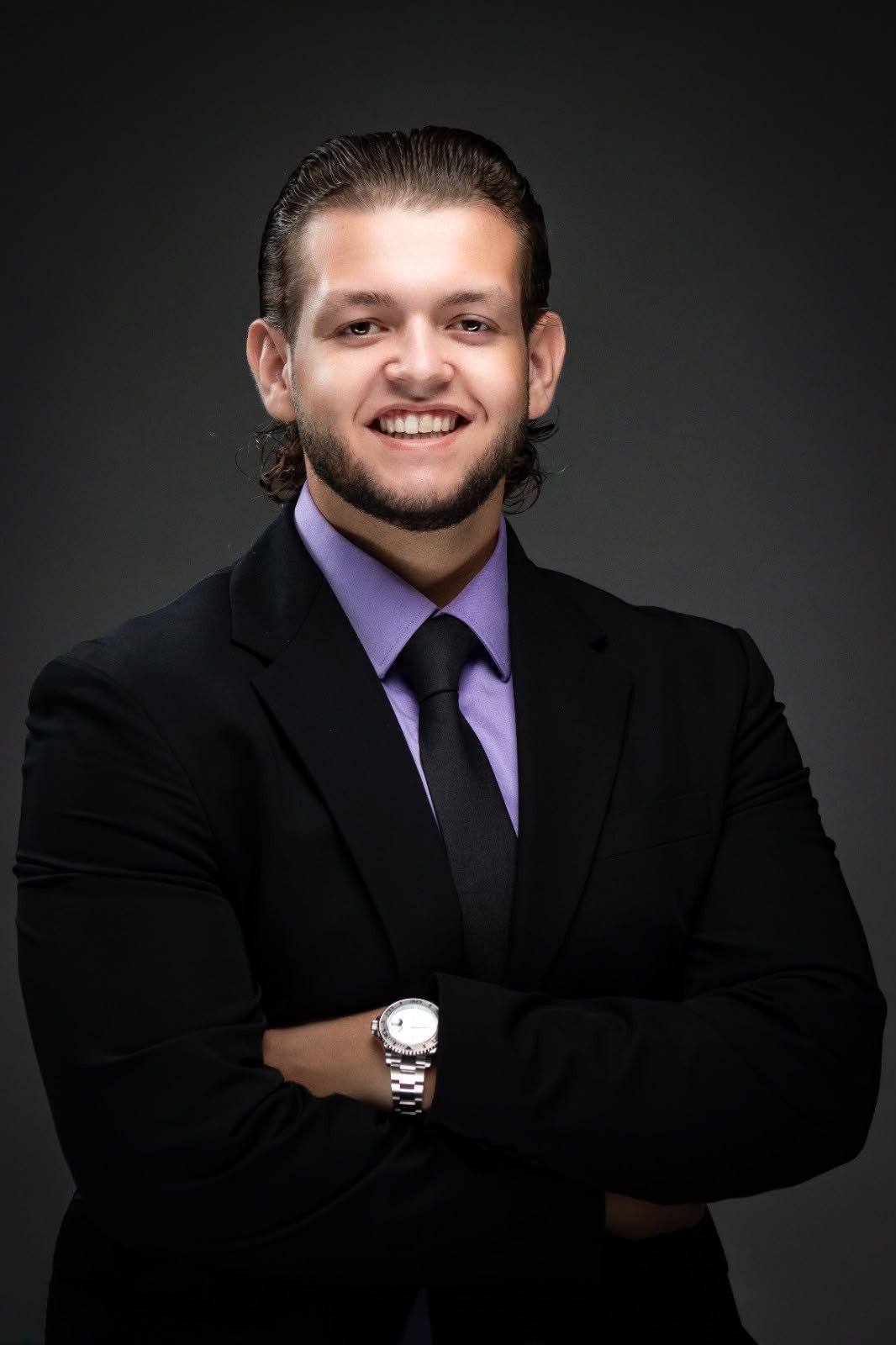 Padrino Visser in a black suit and lilac shirt, arms crossed, smiling